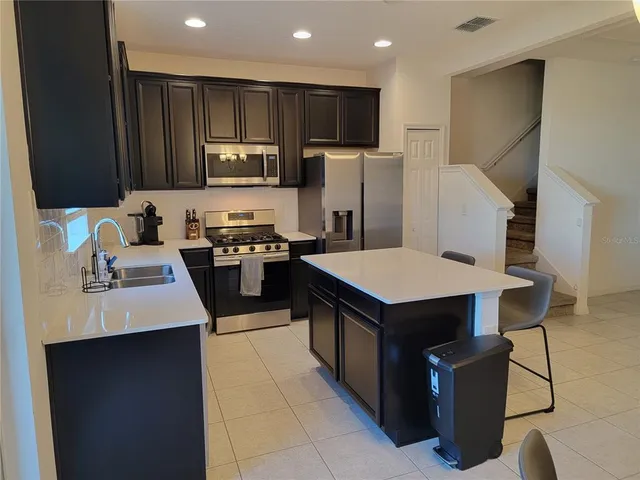 a kitchen with stainless steel appliances kitchen island granite countertop a refrigerator a stove and a sink with wooden cabinets