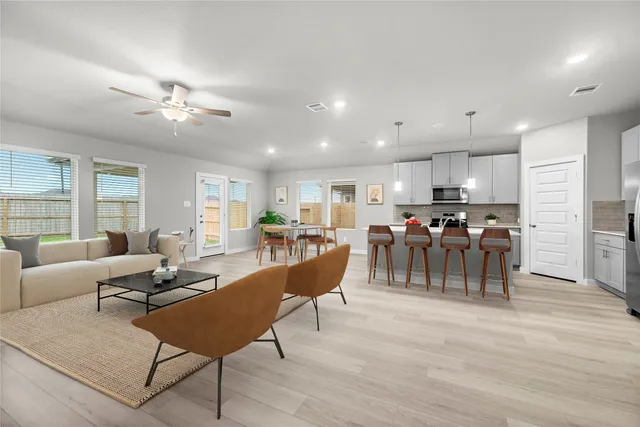 a living room with lots of furniture kitchen view and a wooden floor
