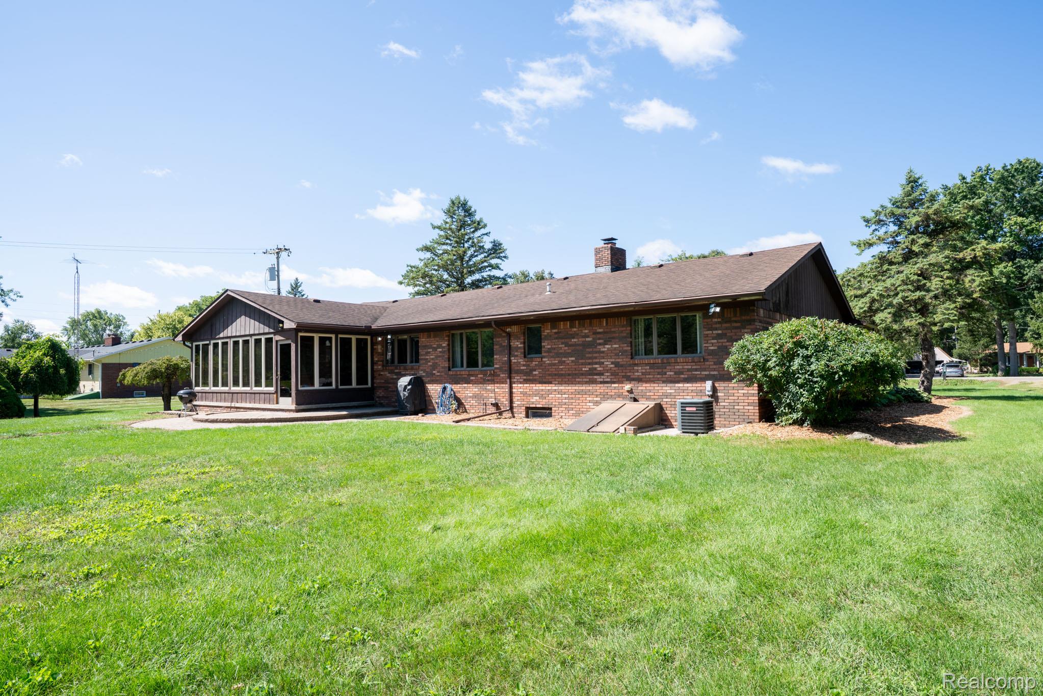 12900 Maxwell Road Carleton, MI 48117 - Photo 17 of 59 Brick exterior with a sunroom addition, large green space, mature trees, and a ground-level patio