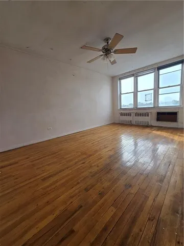 an empty room with wooden floor fan and windows