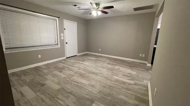 a view of an empty room with wooden floor and a ceiling fan