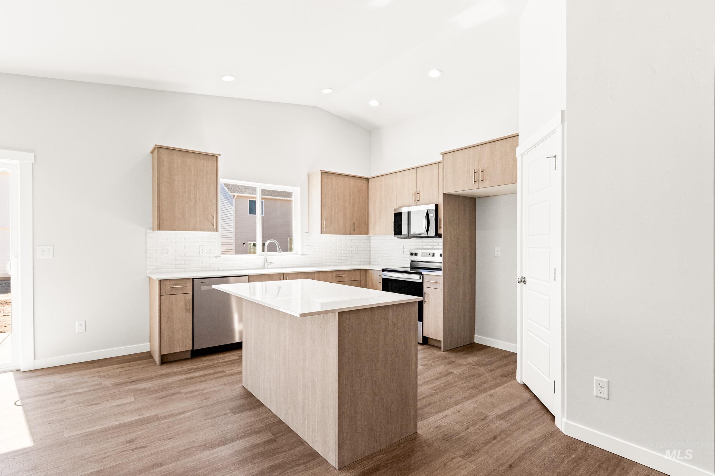 1077 West Jasper Street Meridian, ID 83642 - Photo 3 of 19 Contemporary kitchen featuring light wood-finish cabinetry, a central island with a white countertop, stainless steel appliances, a white subway tile backsplash, and wood-finish flooring