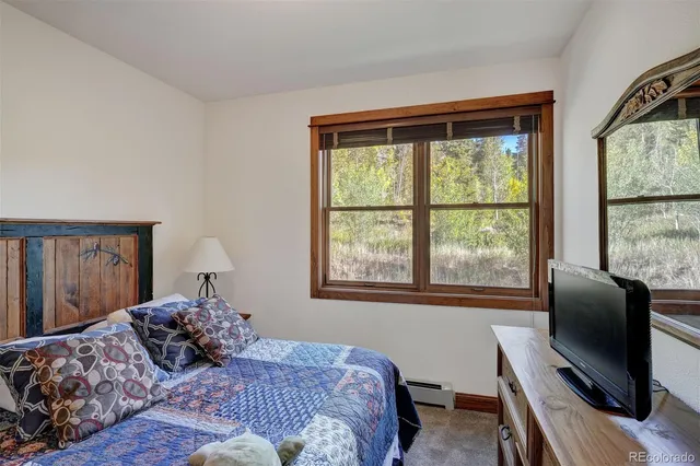 a bedroom with a bed window and a flat tv screen on dresser