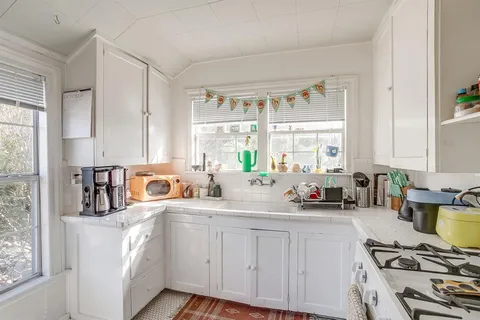 a kitchen with sink a stove and white cabinets