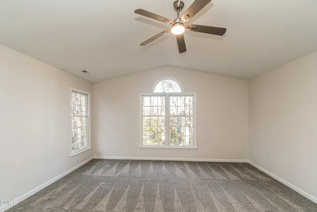 an empty room with chandelier fan and windows