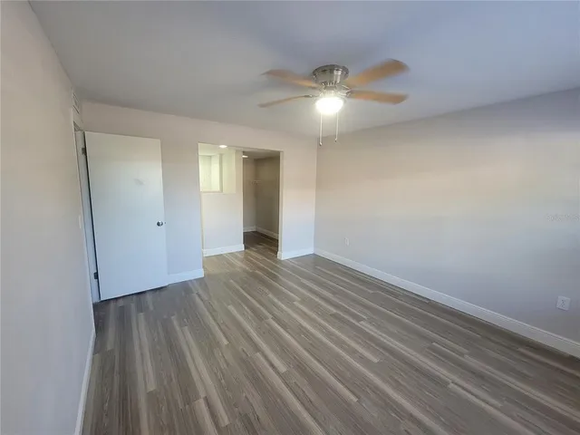 a view of an empty room with wooden floor and a ceiling fan