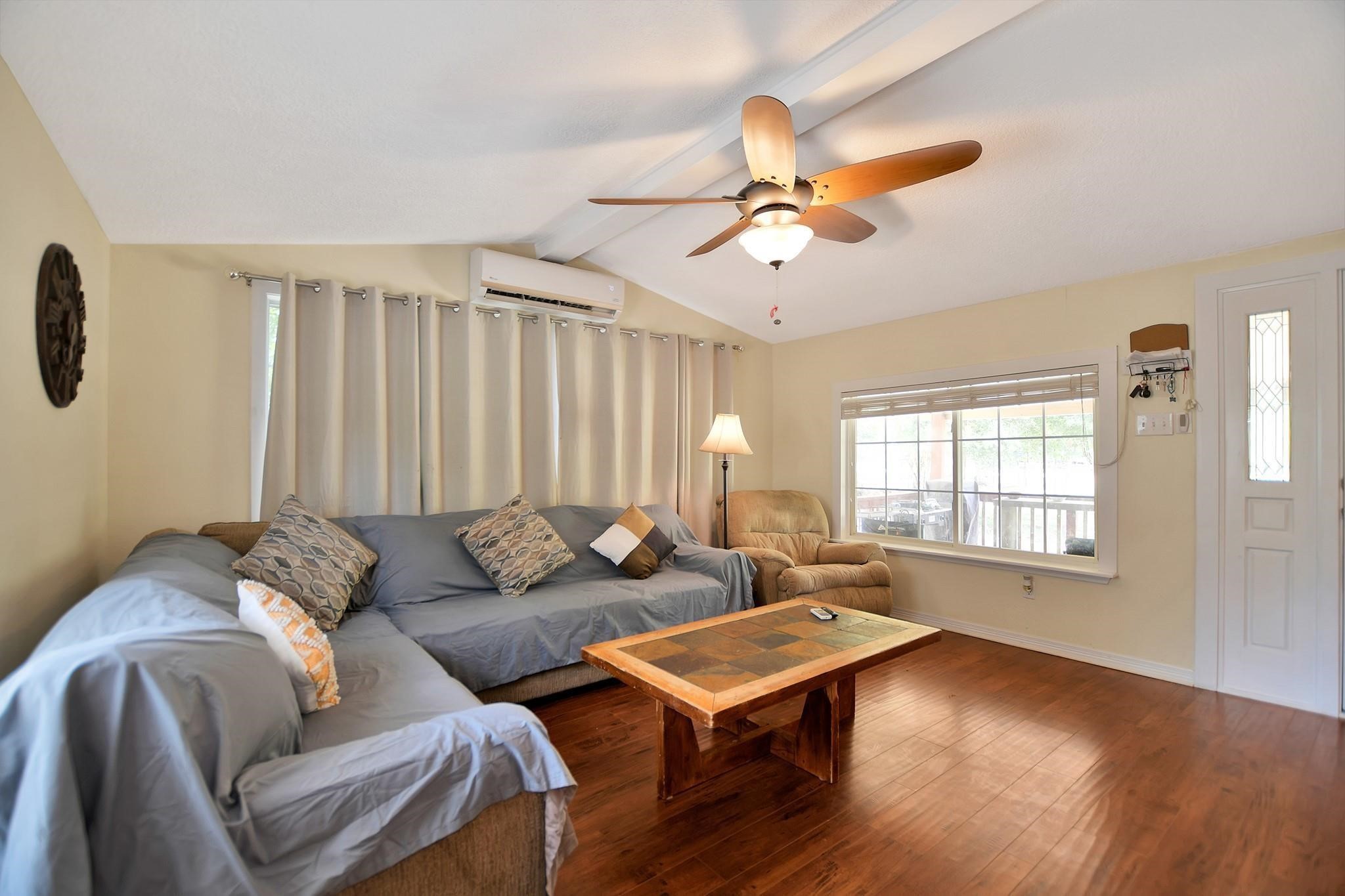 29115 Cherokee Lane Waller, TX 77484 - Photo 12 of 50 This cozy living room features warm wood flooring, a large sectional sofa, and a comfy armchair. It has a ceiling fan, ample natural light from a big window, and an inviting atmosphere perfect for relaxation.
