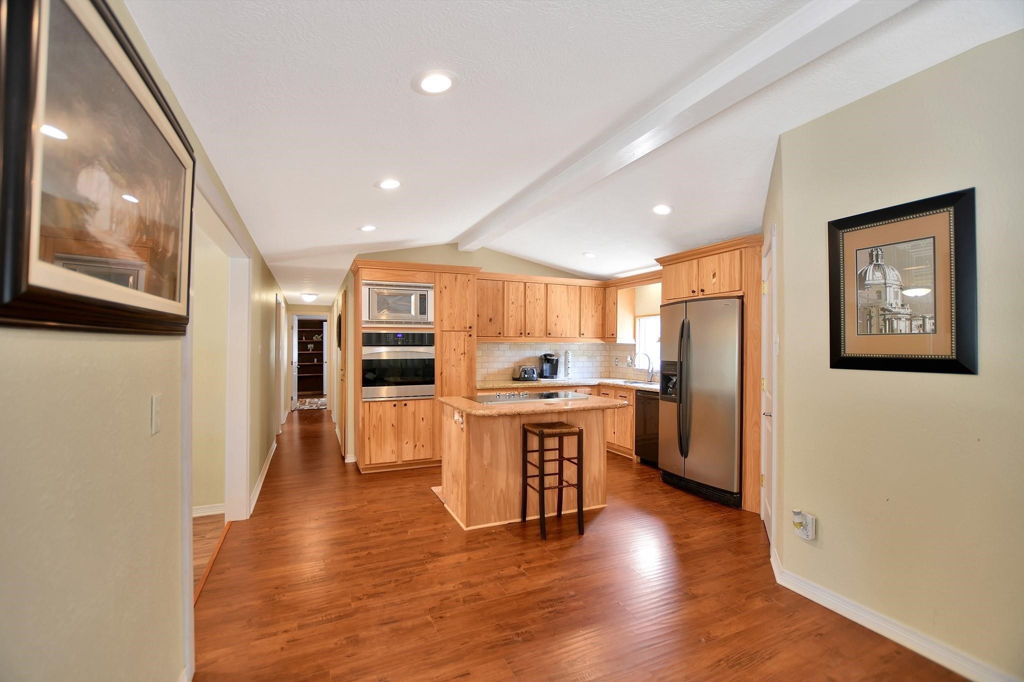 29115 Cherokee Lane Waller, TX 77484 - Photo 14 of 50 This photo showcases a cozy, well-lit kitchen with warm wooden flooring and cabinetry. It features stainless steel appliances, a central island with a stool, and recessed lighting. The space opens into a hallway, creating a welcoming and functional layout.
