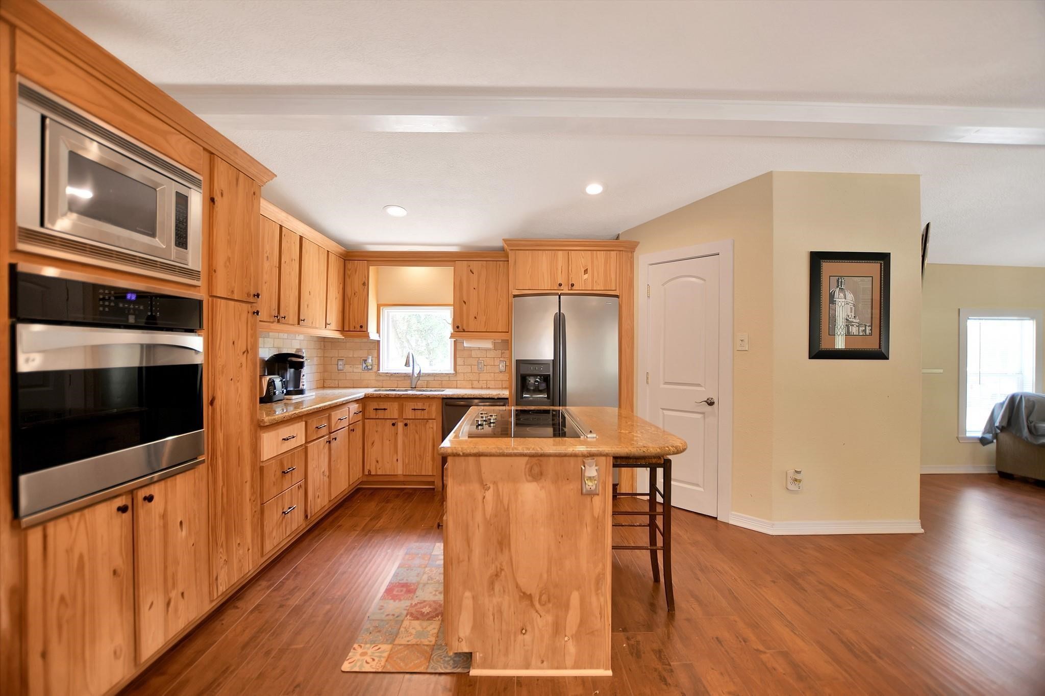 29115 Cherokee Lane Waller, TX 77484 - Photo 15 of 50 This kitchen features warm wooden cabinetry, stainless steel appliances, and a central island with a cooktop. The open layout offers ample natural light and a cozy atmosphere, ideal for family gatherings and entertaining.