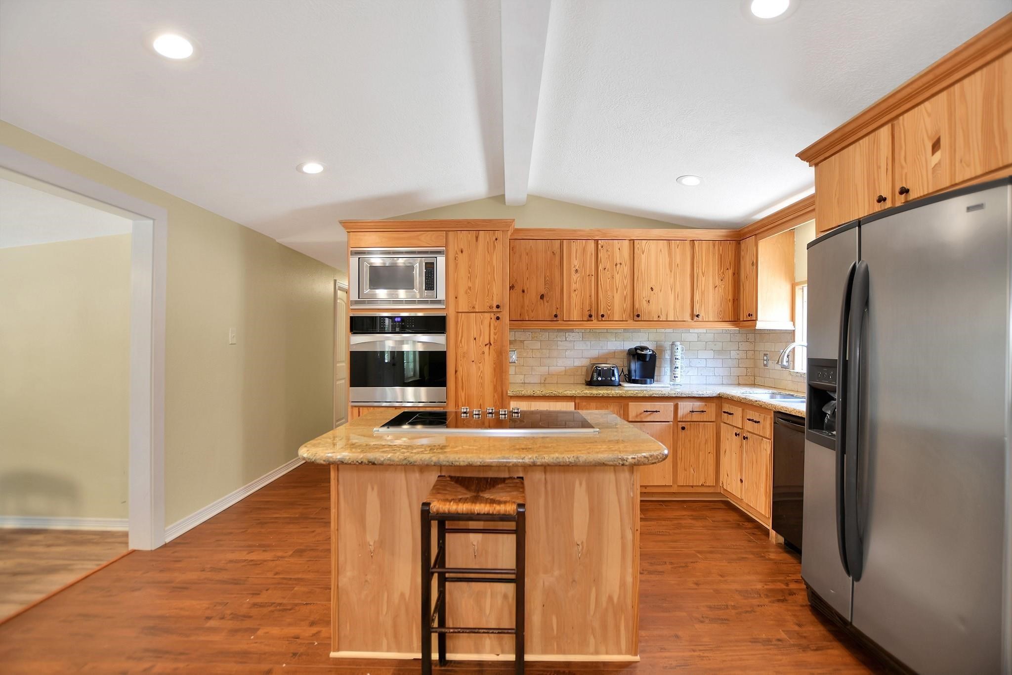 29115 Cherokee Lane Waller, TX 77484 - Photo 17 of 50 This kitchen features natural wood cabinetry, a central island with seating, stainless steel appliances, and a tiled backsplash. It has a warm, inviting atmosphere with recessed lighting and ample counter space.