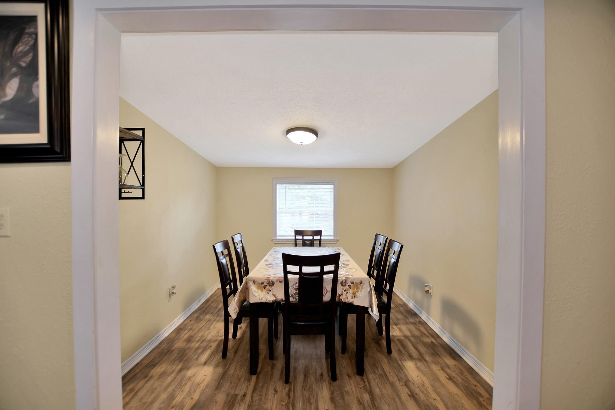 29115 Cherokee Lane Waller, TX 77484 - Photo 19 of 50 This photo shows a cozy dining room with light-colored walls and wood flooring. It features a rectangular table with six chairs, centered under a ceiling light, and a window providing natural light.