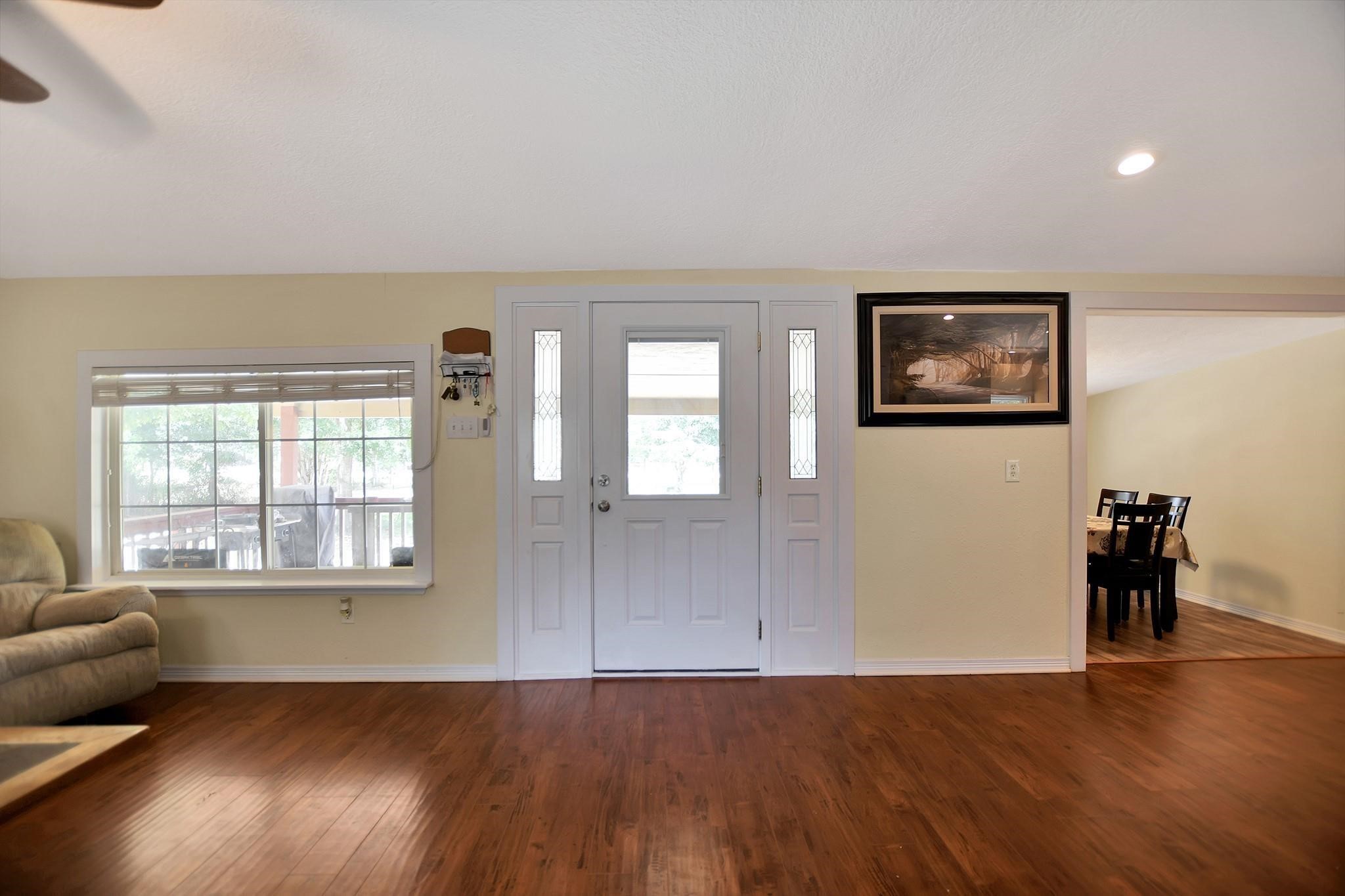 29115 Cherokee Lane Waller, TX 77484 - Photo 20 of 50 Bright living area with hardwood floors, a large window, and a white front door. The space is open to a dining room, creating a welcoming and spacious atmosphere.
