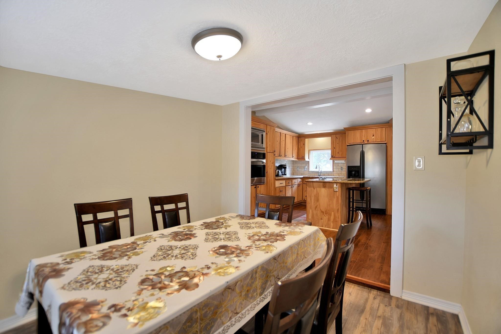 29115 Cherokee Lane Waller, TX 77484 - Photo 21 of 50 This photo shows a cozy dining area connected to a modern kitchen. The dining room features a table with seating for six, and the kitchen has wooden cabinetry, stainless steel appliances, and a central island with bar stools, creating a warm and inviting space for meals and gatherings.