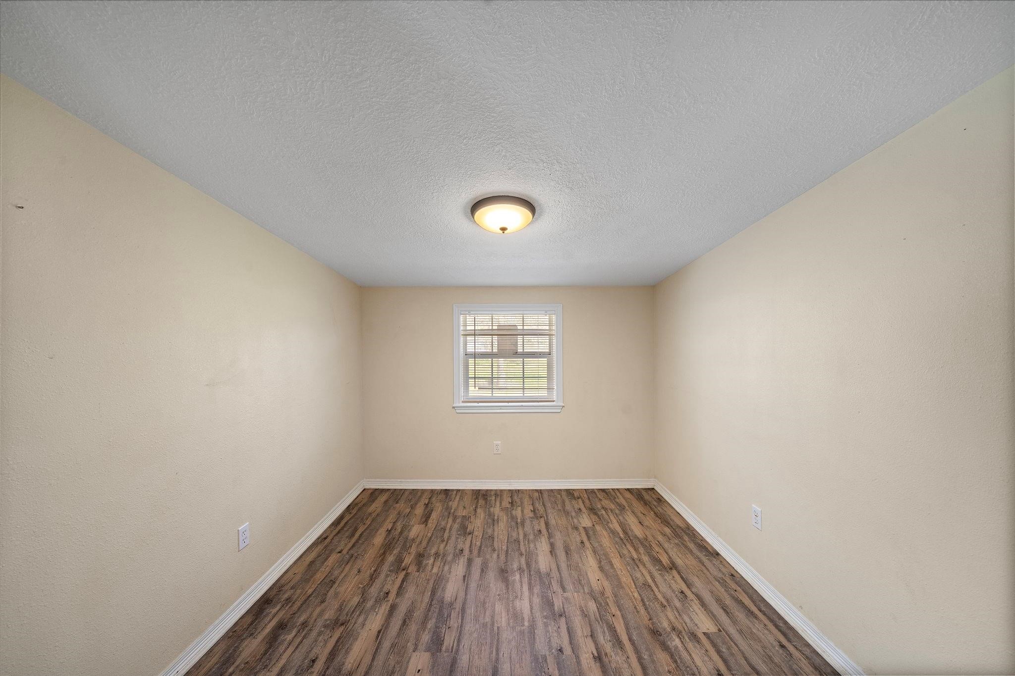 29115 Cherokee Lane Waller, TX 77484 - Photo 22 of 50 This room features a cozy, narrow layout with light beige walls and wood-look flooring. A central ceiling light and a single window provide ample lighting, making it a bright and inviting space.