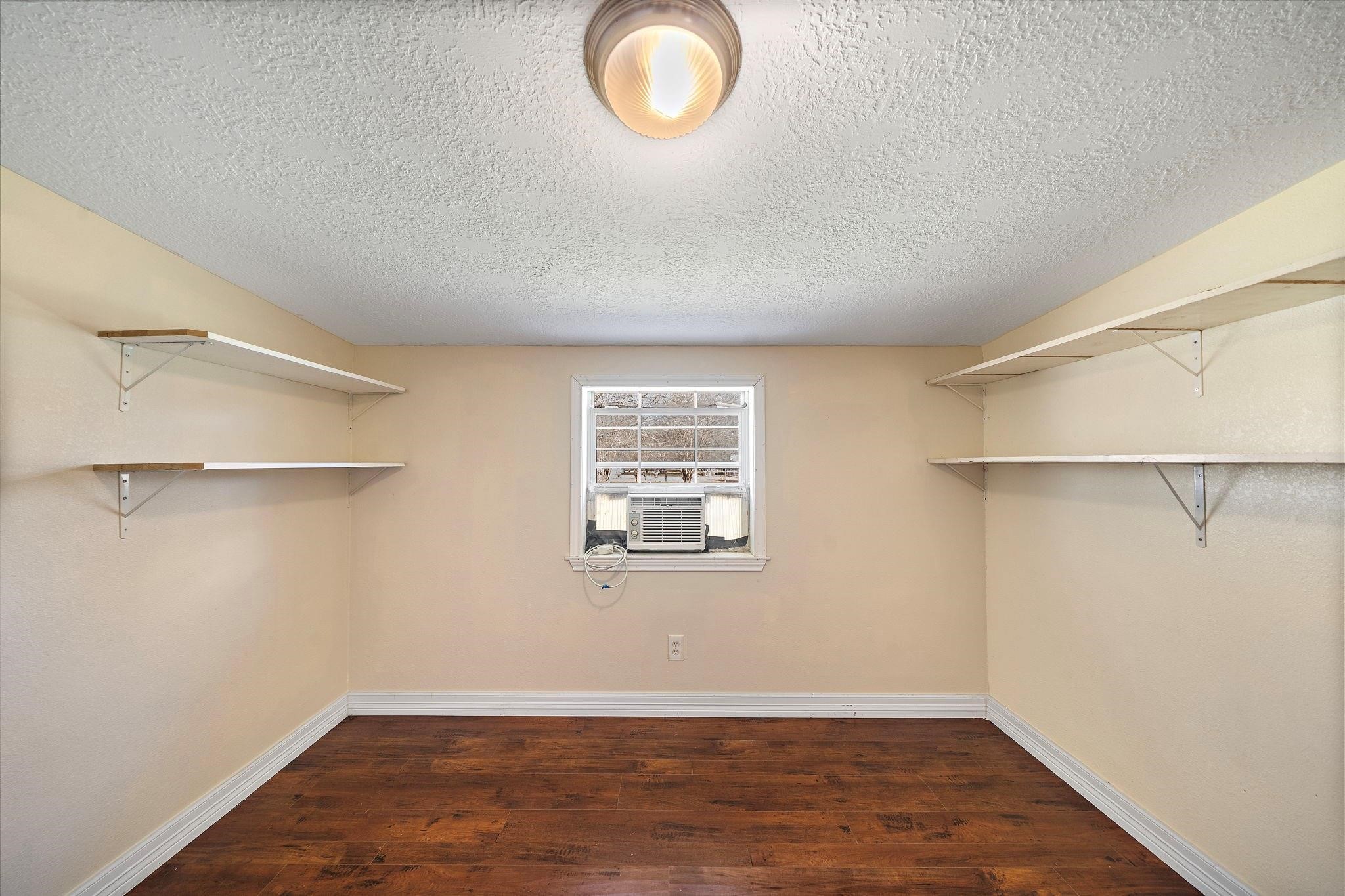 29115 Cherokee Lane Waller, TX 77484 - Photo 27 of 50 This room features a compact space with wooden flooring, neutral-toned walls, and built-in shelves on both sides. A window with an air conditioning unit provides natural light and ventilation. Ideal for use as a small office or storage area.