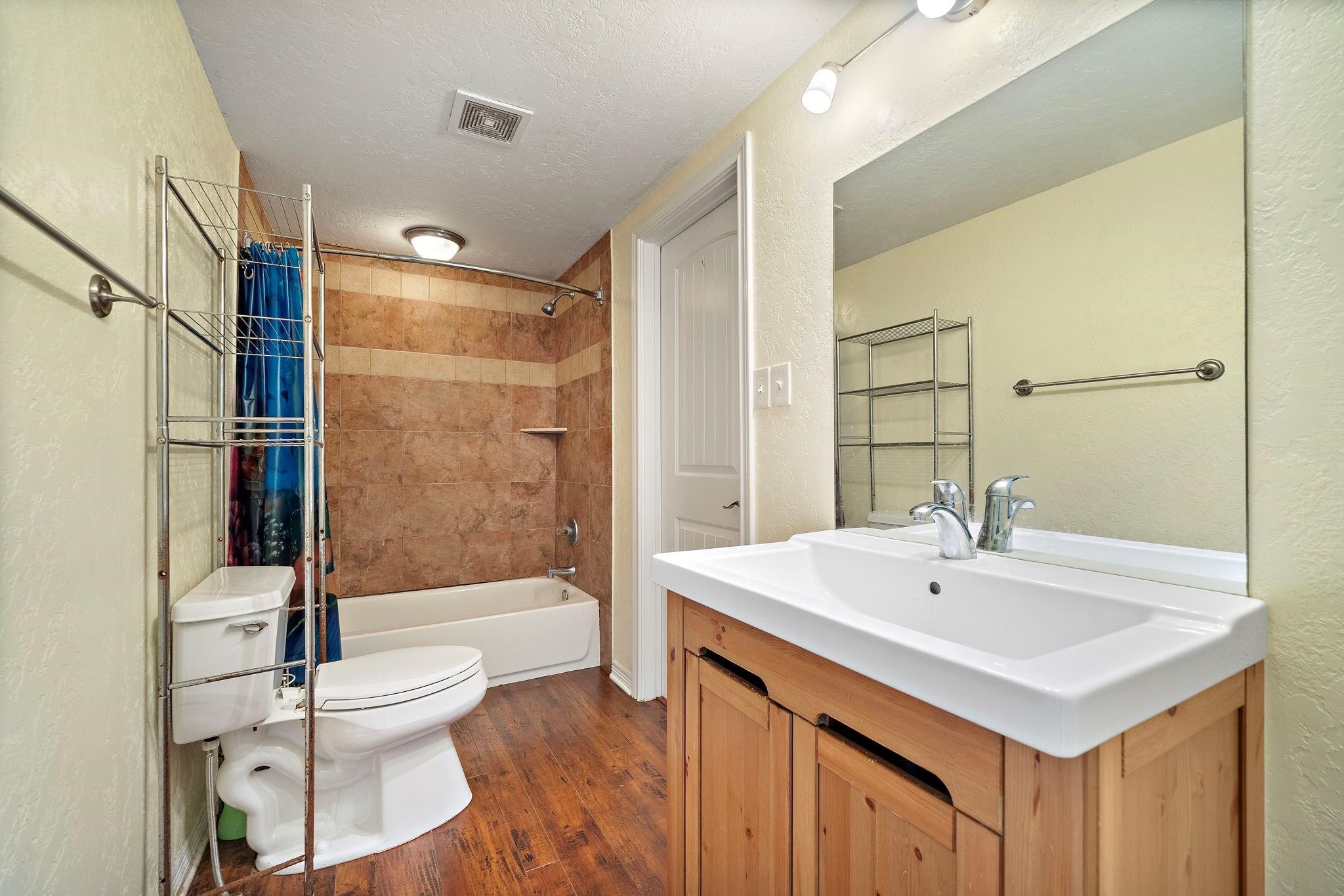 29115 Cherokee Lane Waller, TX 77484 - Photo 28 of 50 This bathroom features a modern design with a warm color palette. It includes a bathtub with tiled walls, a sleek vanity with a large mirror, and wood-style flooring. Ample lighting and storage options enhance its functionality.