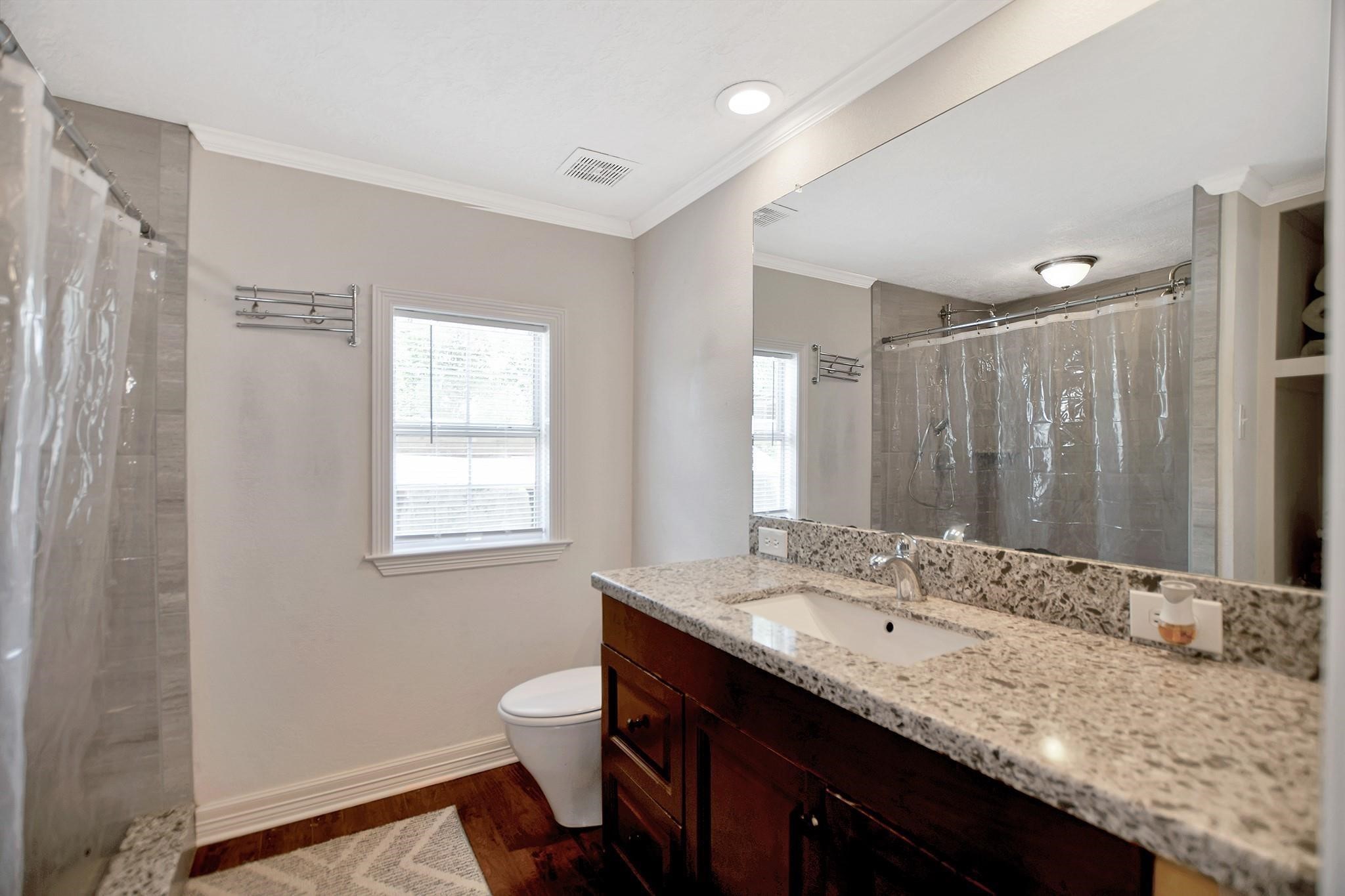 29115 Cherokee Lane Waller, TX 77484 - Photo 29 of 50 This bathroom features a modern design with a granite countertop, single sink, and a large mirror. It includes a bathtub with a shower, neutral-toned walls, and wood flooring, creating a clean and inviting space.