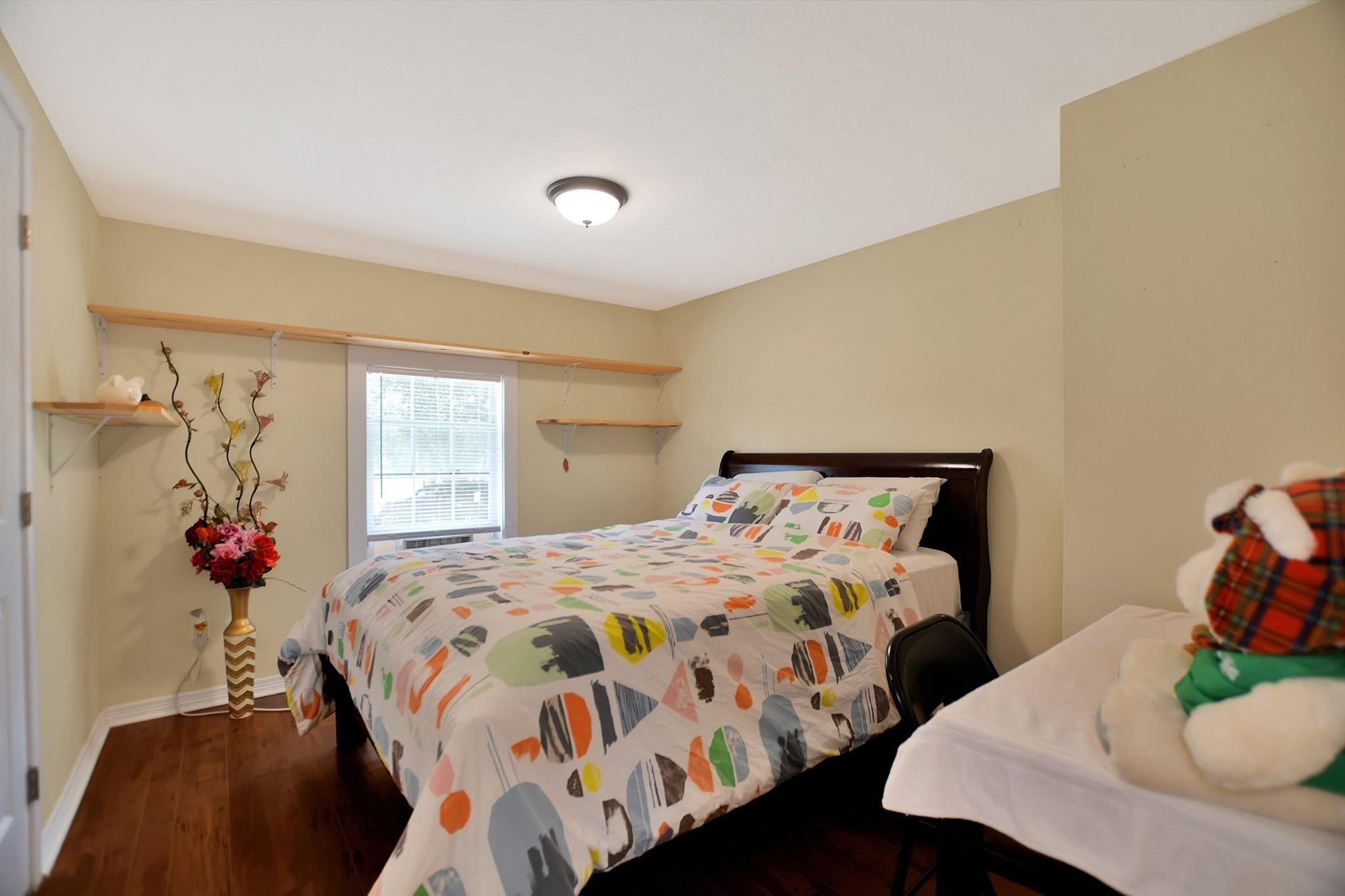 29115 Cherokee Lane Waller, TX 77484 - Photo 32 of 50 Cozy bedroom with a large window allowing natural light, featuring warm beige walls and hardwood flooring. The room includes a bed with colorful bedding, a small table, and decorative shelves with floral accents.