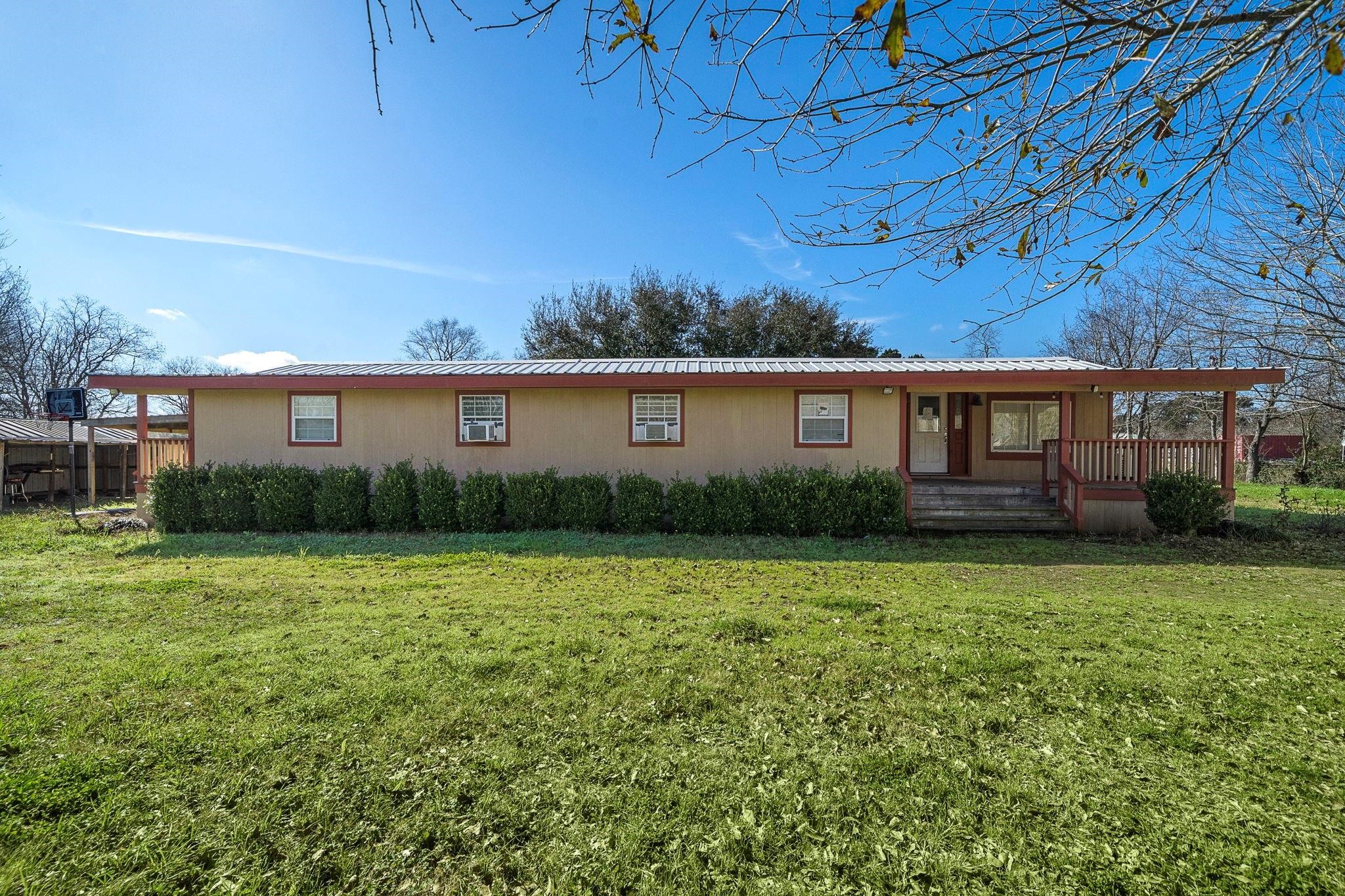 29115 Cherokee Lane Waller, TX 77484 - Photo 37 of 50 This photo showcases a charming one-story home with a metal roof and a welcoming front porch. The property is surrounded by a spacious, well-maintained lawn and mature trees, offering a serene and private setting.