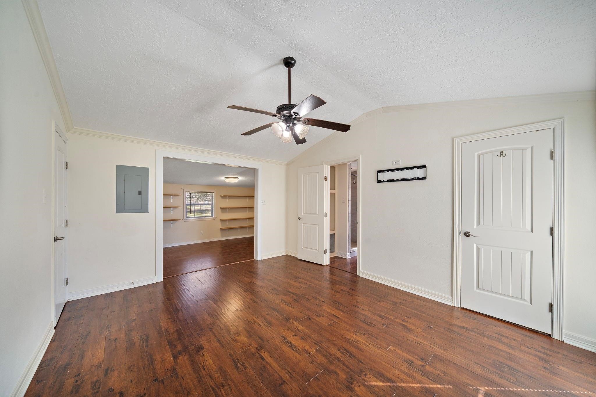 29115 Cherokee Lane Waller, TX 77484 - Photo 4 of 50 This photo shows a bright, open room with hardwood floors and a ceiling fan. It features two doors and an open doorway leading to another room with built-in shelves and a window, allowing natural light to fill the space.