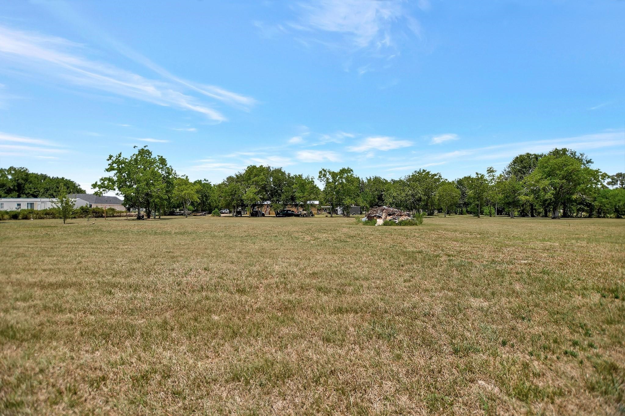 29115 Cherokee Lane Waller, TX 77484 - Photo 42 of 50 Expansive grassy lot with scattered trees and a clear sky, offering ample space and potential for development in a peaceful setting.