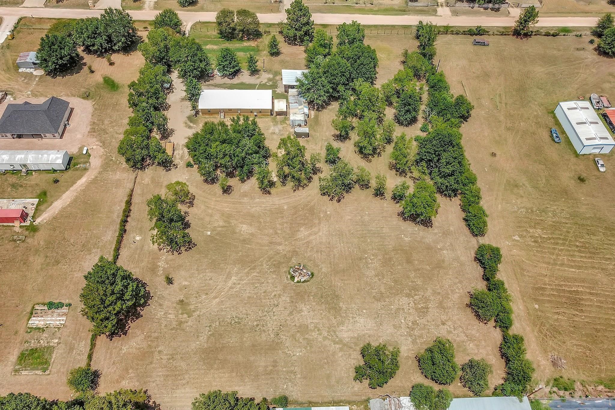 29115 Cherokee Lane Waller, TX 77484 - Photo 46 of 50 This aerial photo showcases a spacious property with a mix of open land and mature trees. A central house is surrounded by greenery, offering privacy. The expansive yard provides ample space for outdoor activities, gardening, or potential development. Nearby structures suggest a rural or semi-rural setting, perfect for those seeking tranquility and space.