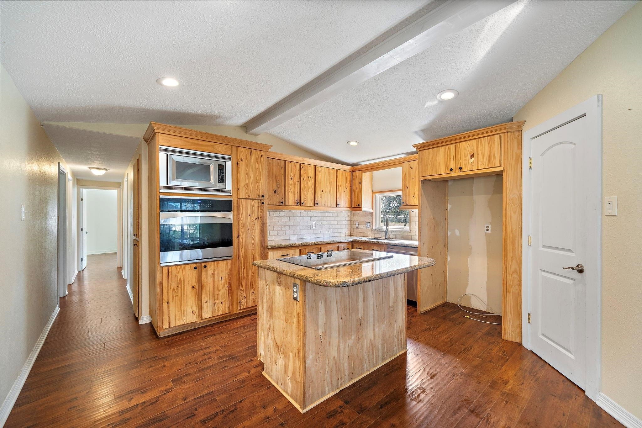 29115 Cherokee Lane Waller, TX 77484 - Photo 5 of 50 This kitchen features rustic wooden cabinetry, a central island with a cooktop, and stainless steel appliances. The space is well-lit with recessed lighting and has a warm, inviting hardwood floor.