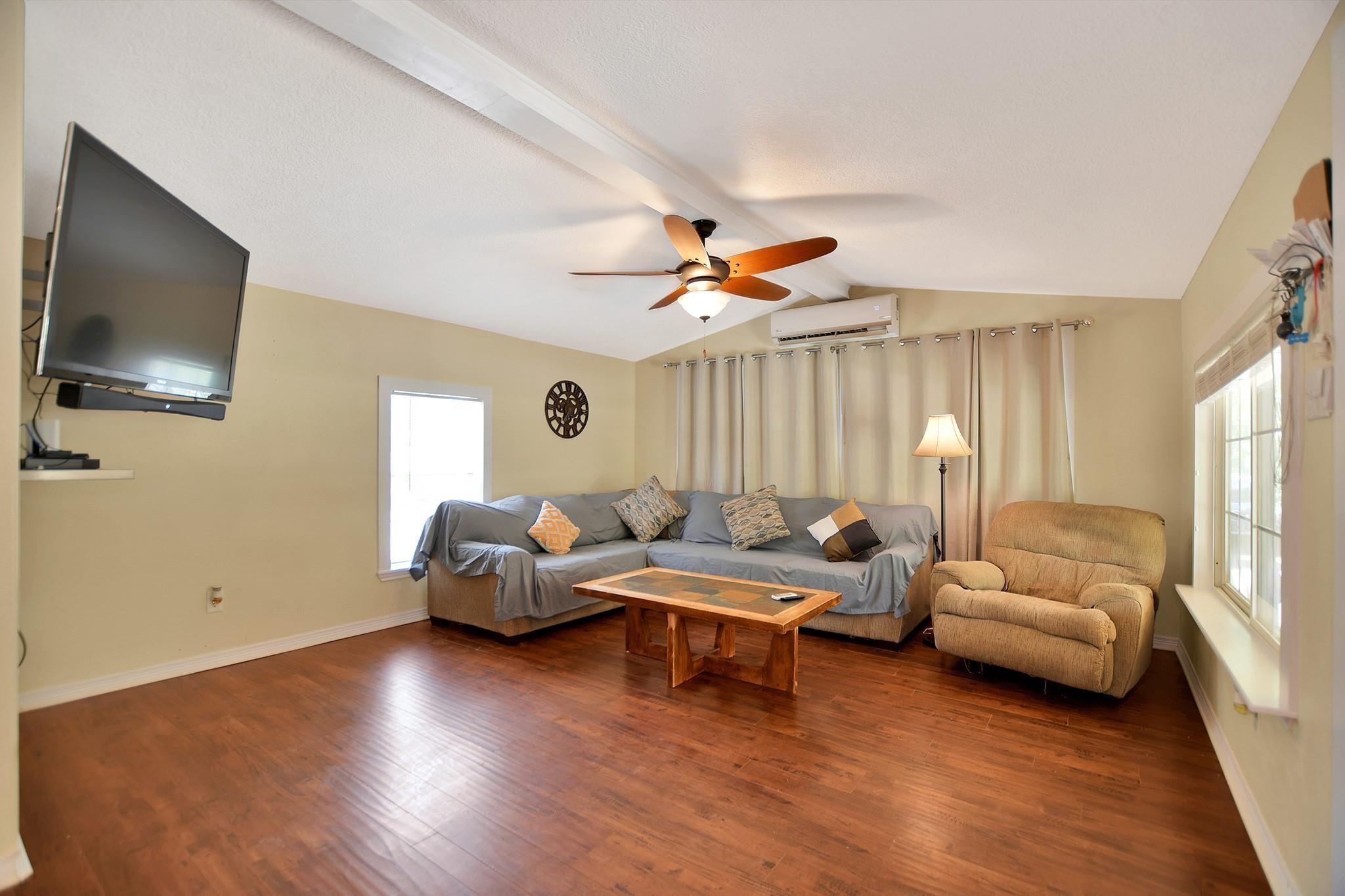 29115 Cherokee Lane Waller, TX 77484 - Photo 8 of 50 This cozy living room features hardwood floors, a ceiling fan, and ample natural light. It includes a mounted TV, comfortable seating with a large sofa and armchair, and a coffee table, making it perfect for relaxation and entertainment.