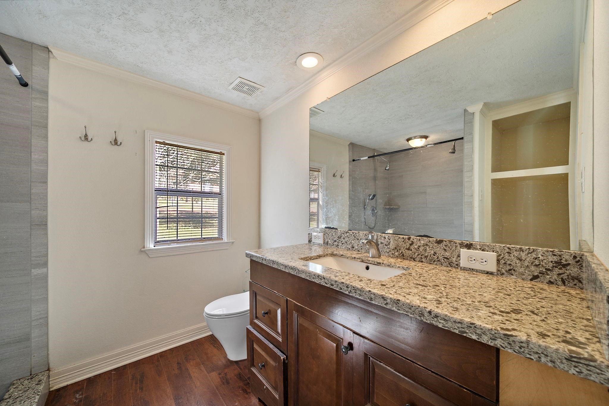 29115 Cherokee Lane Waller, TX 77484 - Photo 9 of 50 This bathroom features a granite countertop with a single sink, wooden cabinetry, and a large mirror. It has a walk-in shower with modern fixtures, a window for natural light, and a classic wooden floor.