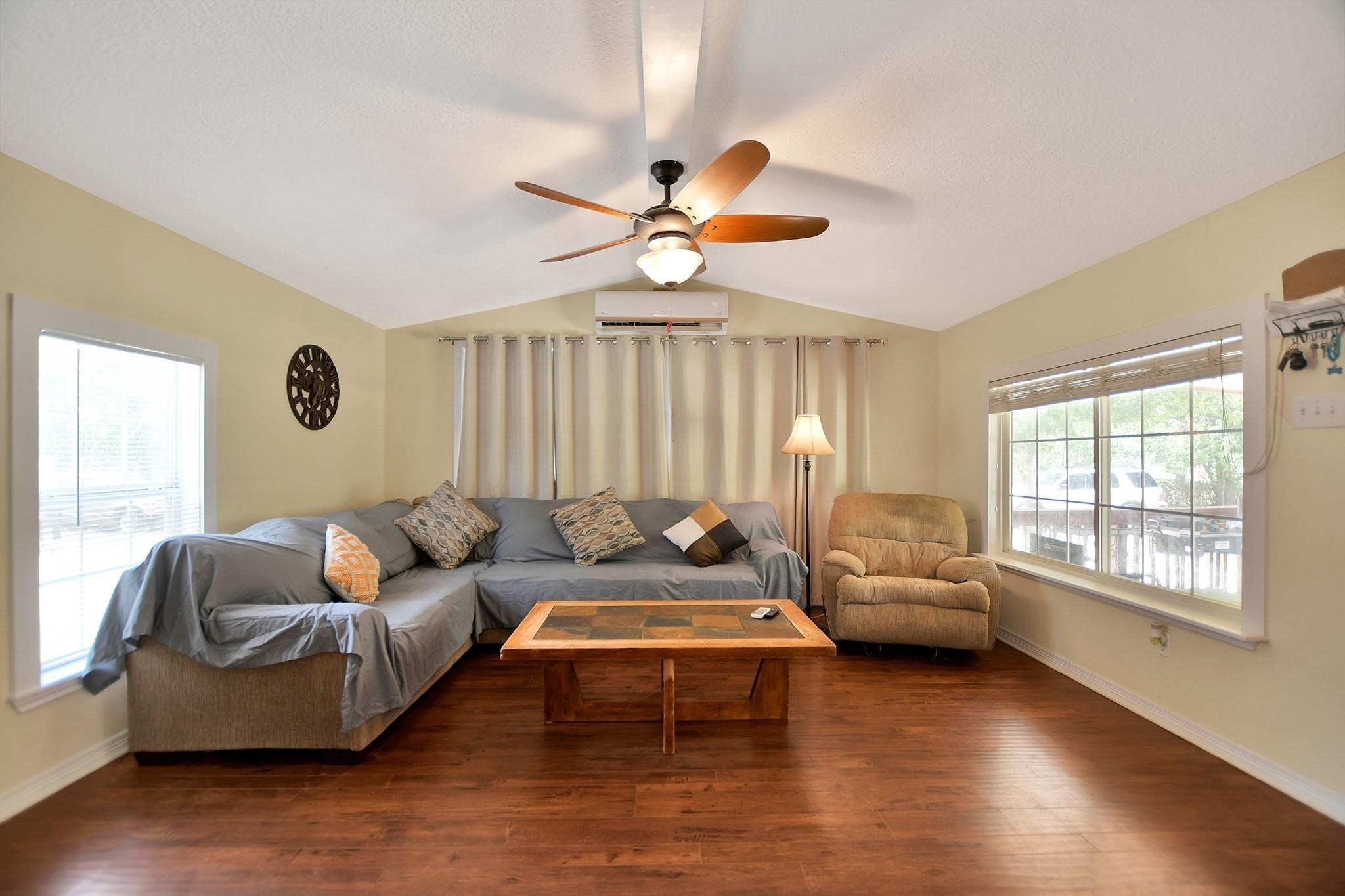 29115 Cherokee Lane Waller, TX 77484 - Photo 10 of 50 This cozy living room features hardwood floors, a ceiling fan, and ample natural light from large windows. It includes a comfortable sectional sofa, an armchair, and a stylish coffee table, making it perfect for relaxing or entertaining.