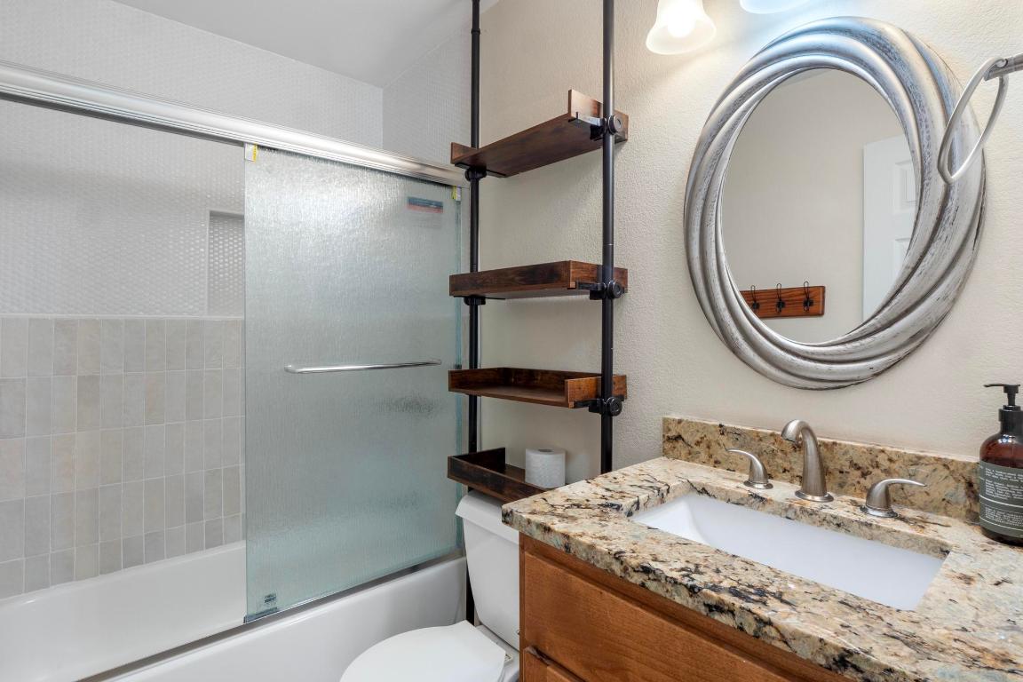 10213 Thomas Lane Dripping Springs, TX 78620 - Photo 24 of 40 a bathroom with a granite countertop sink a mirror and a shower