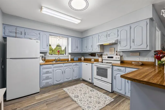 a kitchen with granite countertop a refrigerator a sink dishwasher a stove and white cabinets with wooden floor