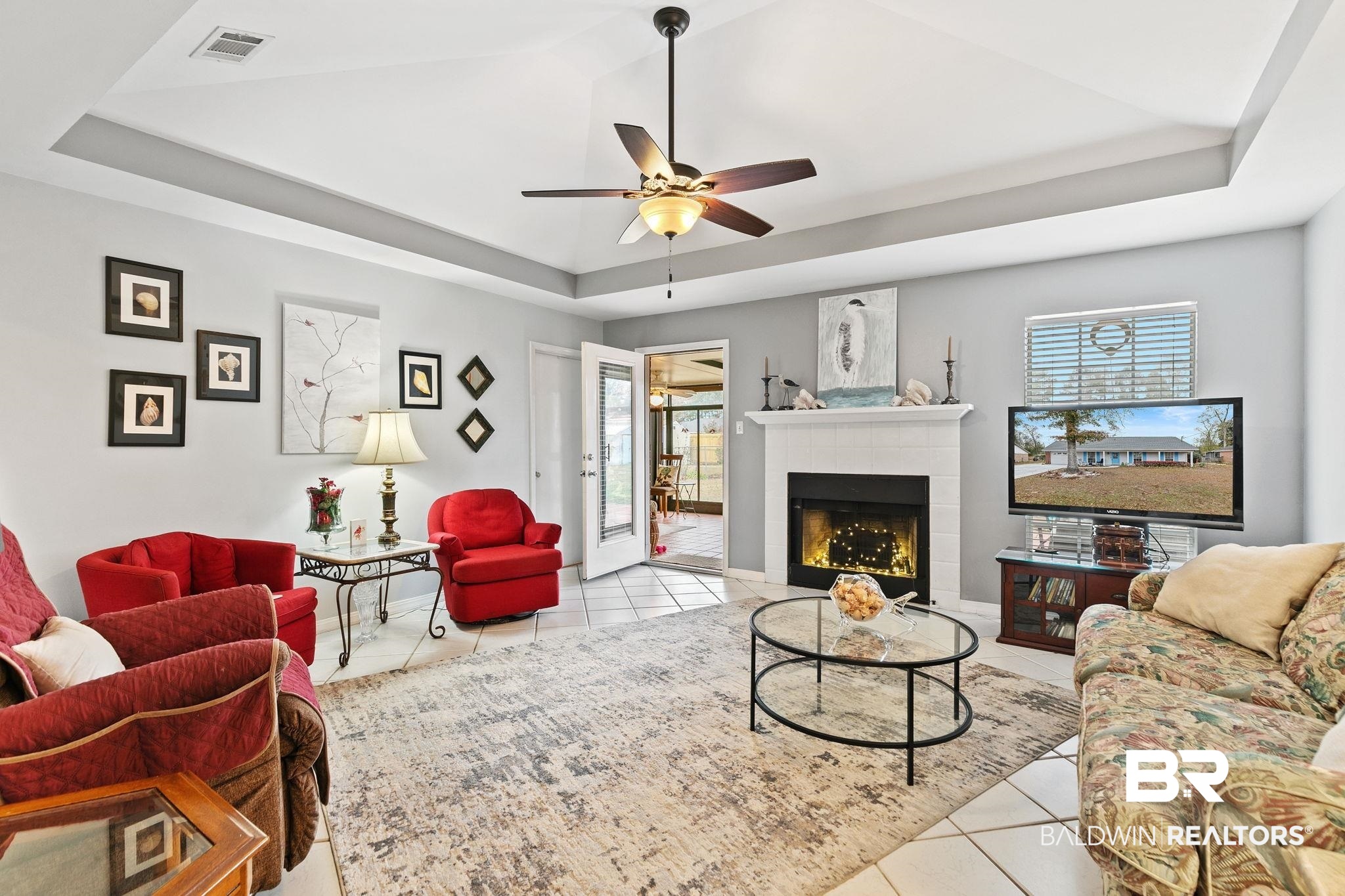 519 Juniper Place Drive Foley, AL 36535 - Photo 10 of 47 Living area with a tray ceiling, a tiled fireplace, light tile patterned floors, and a ceiling fan