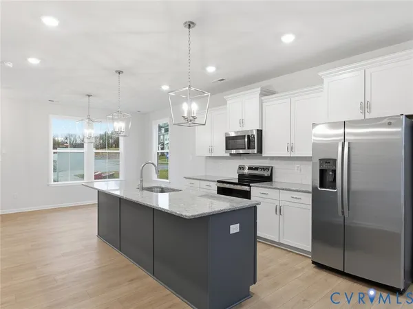 a kitchen with stainless steel appliances granite countertop a refrigerator a sink dishwasher a oven and a dining table with wooden floor