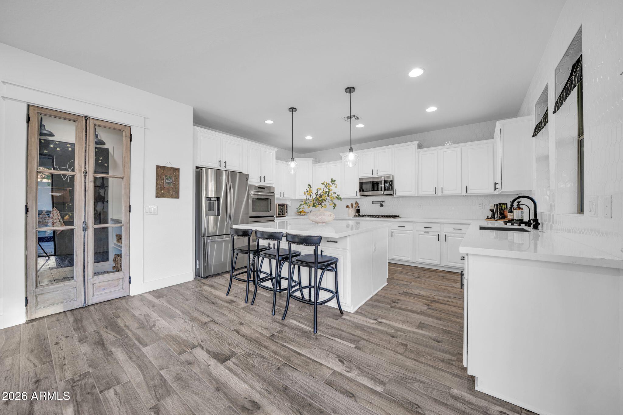 2985 North Point Ridge Road Buckeye, AZ 85396 - Photo 56 of 107 a kitchen with stainless steel appliances kitchen island granite countertop a refrigerator a stove top oven a sink and white cabinets with wooden floor