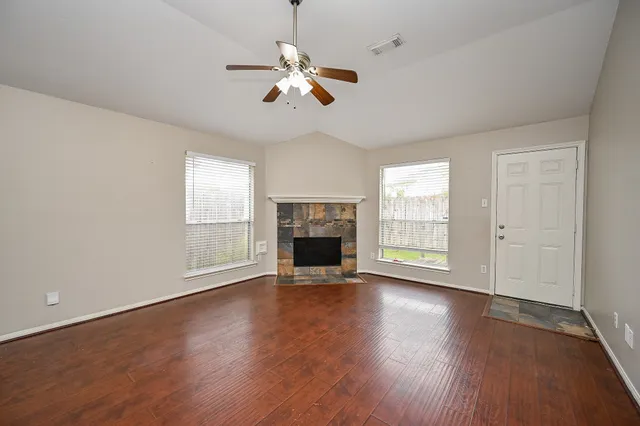 a view of an empty room with wooden floor fireplace and a window