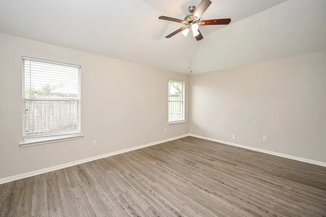 an empty room with wooden floor fan and windows