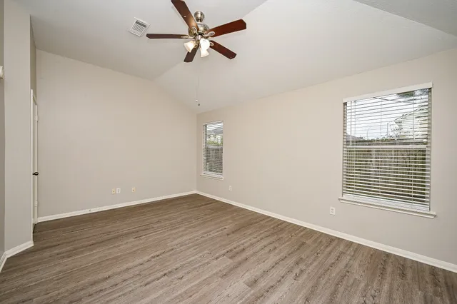 an empty room with wooden floor fan and windows