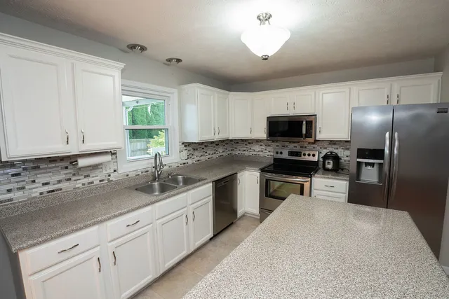 a kitchen with granite countertop a sink stainless steel appliances and white cabinets