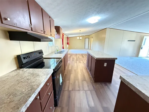 a kitchen with granite countertop a sink a stove top oven a counter space and cabinets