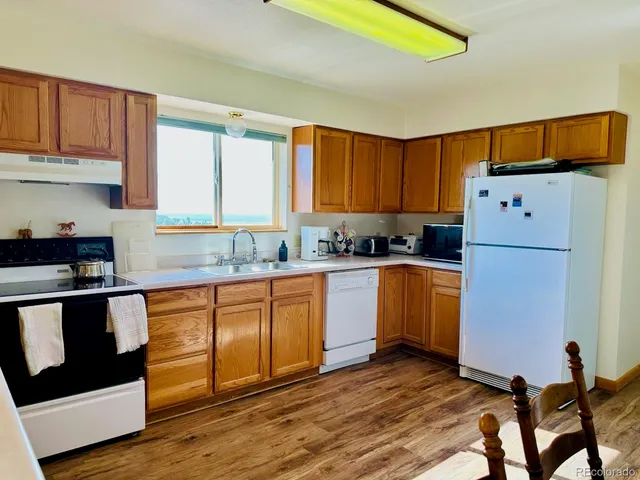 a kitchen with granite countertop a refrigerator a stove a sink dishwasher and wooden cabinets with wooden floor