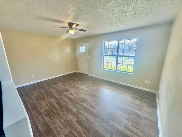 an empty room with wooden floor fan and windows