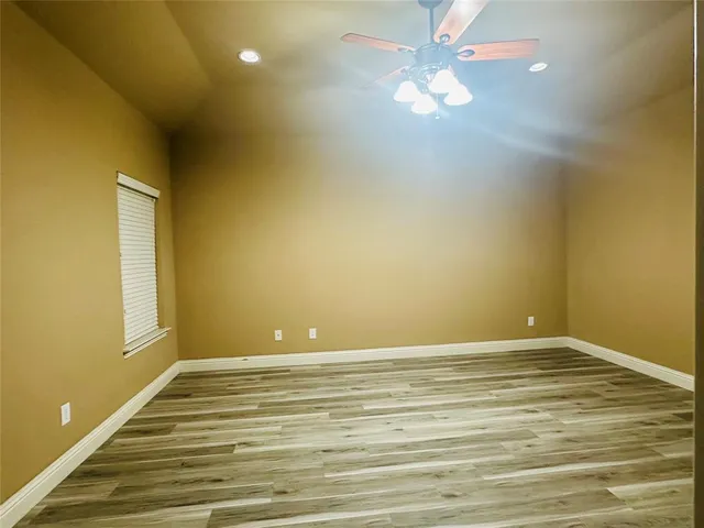 a view of an empty room with wooden floor and a ceiling fan
