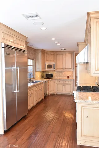 a kitchen with granite countertop a refrigerator oven a sink dishwasher and white cabinets with wooden floor