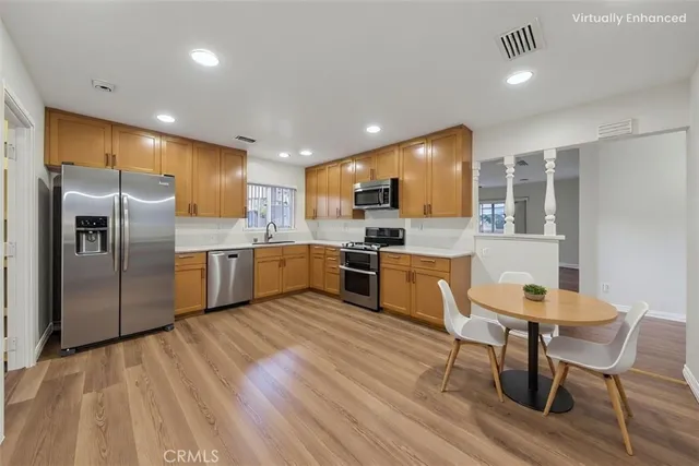 a kitchen with stainless steel appliances a refrigerator a stove top oven a sink dishwasher a dining table and chairs with wooden floor