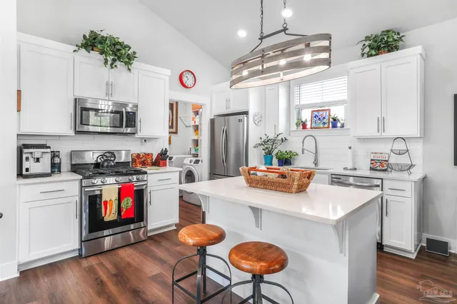 a kitchen with stainless steel appliances granite countertop a stove a refrigerator a sink dishwasher and white cabinets with wooden floor