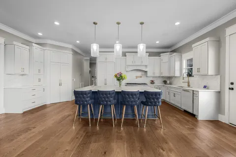 a kitchen with stainless steel appliances granite countertop a white table chairs and a wooden floor