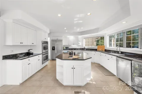 a large white kitchen with granite countertop a sink and dishwasher a stove top oven with wooden floor