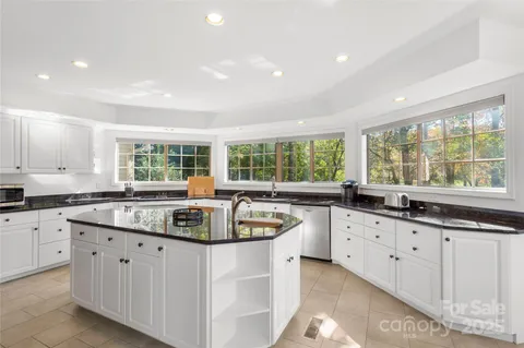 a kitchen with granite countertop a stove a sink a refrigerator and white cabinets with wooden floor