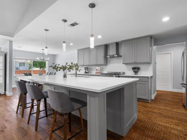 a kitchen with kitchen island a sink a stove a refrigerator and a dining table with wooden floor